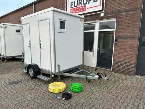 Toiletwagen 1+1, met waterslang, afvoerslang en stroomkabel op de grond ervoor