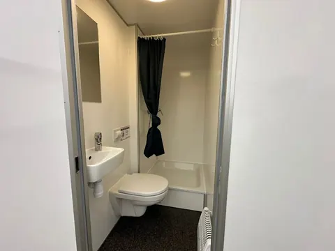 Dubbele mobiele badkamer, badkamerruimte met wandtoilet, kleine wastafel, spiegel en douche met gordijn