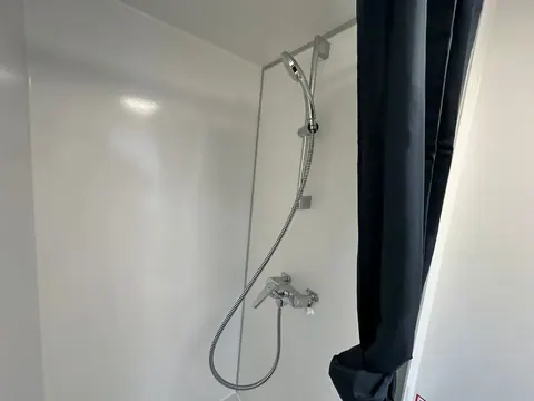 Dubbele mobiele badkamer, douche met handdouche aan een glijstang en een donker douchegordijn