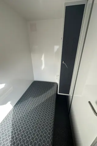 Mobiele woonunit 570 2A, kleine lichte ruimte met een smalle matras en een hoge kast ernaast